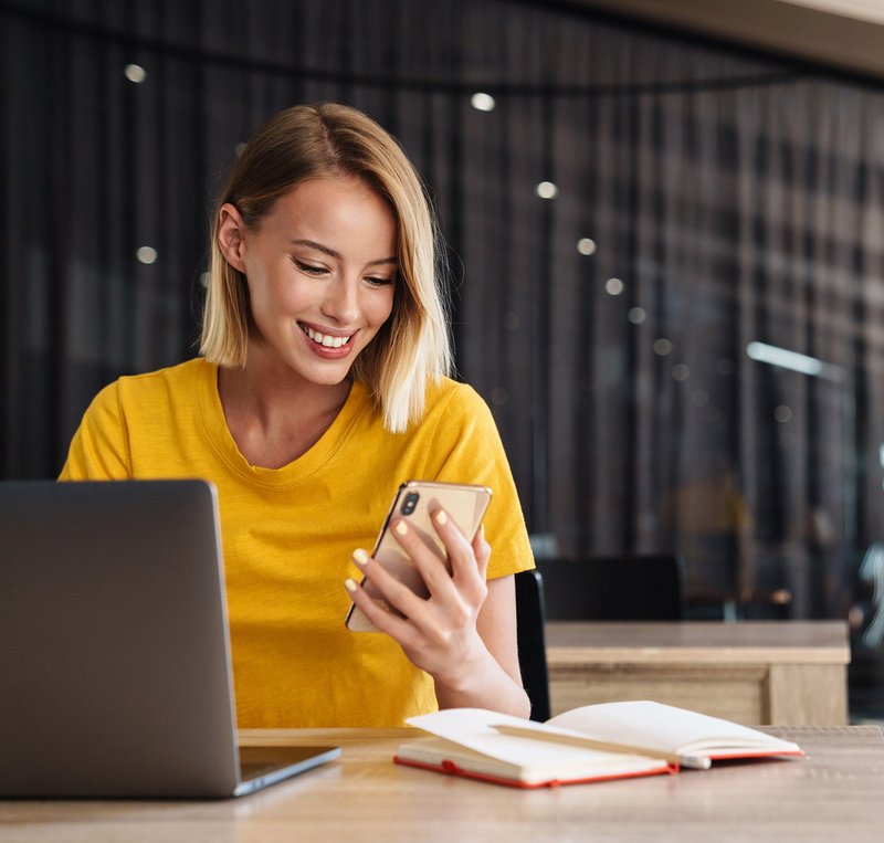 Frau mit mit gelbem Shirt loggt sich an einem Computer ein mit Hilfe ihres Mobiles